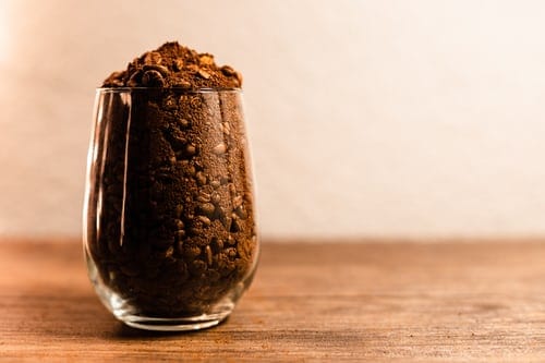 A glass full of non-uniform coffee beans and grounds