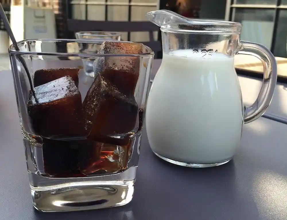 Coffee ice cubes in a glass and a pitcher full of half and half ready to be served.