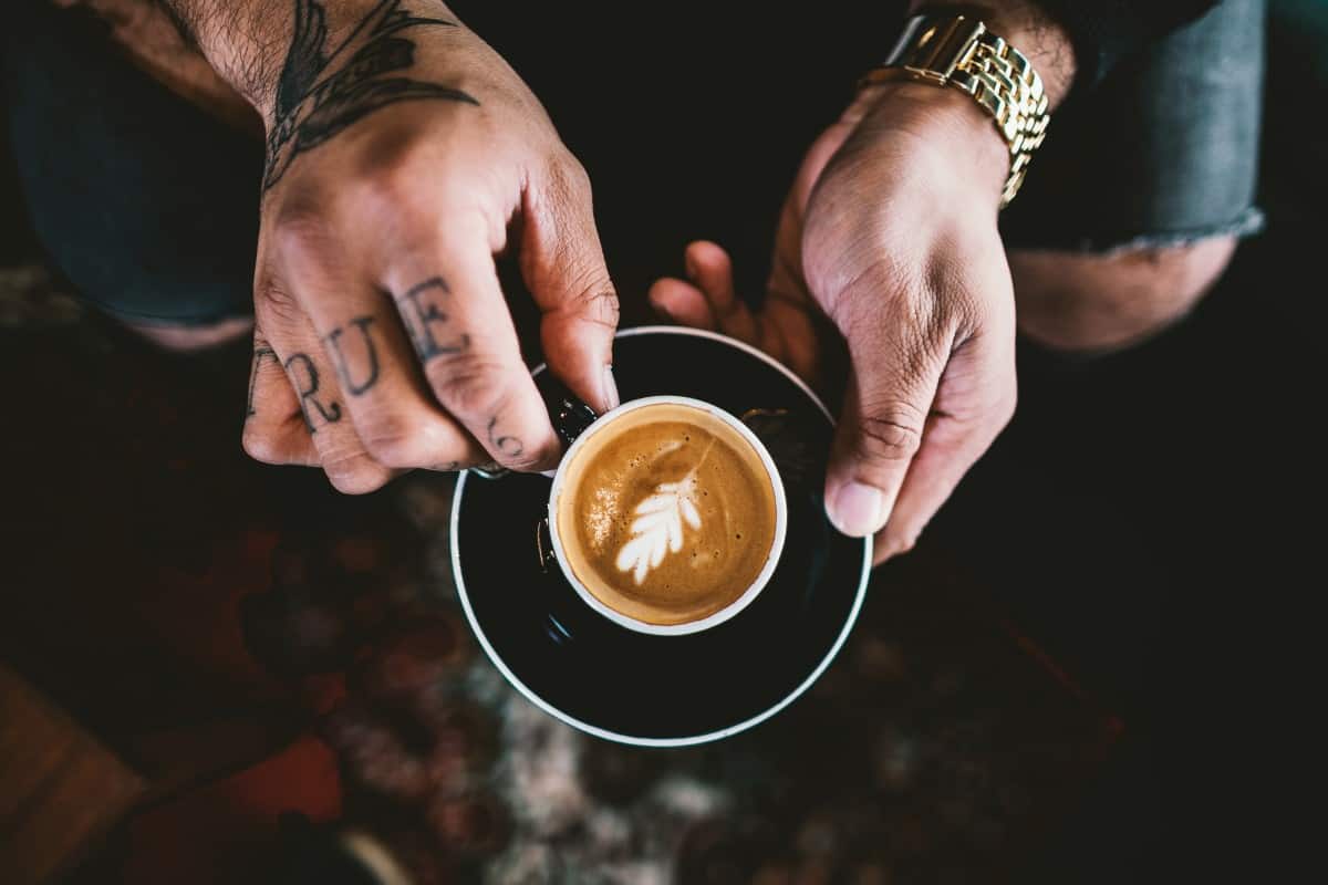 a man with tattoos holding a cup of coffee in his hands