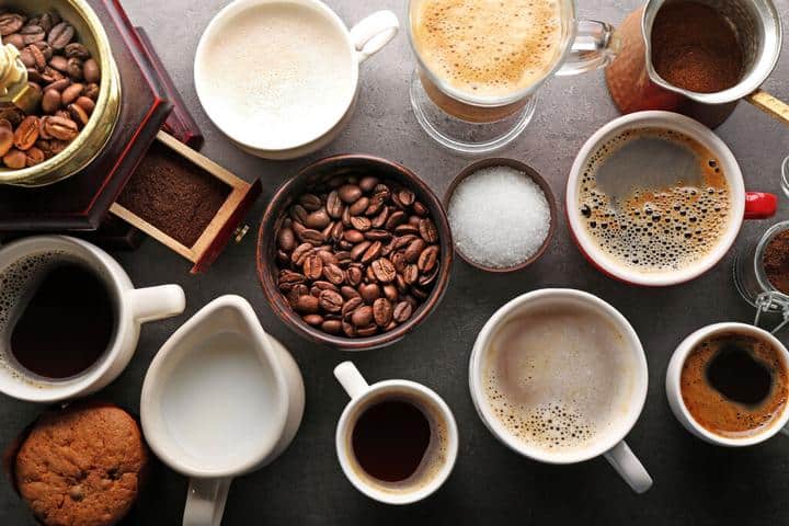 An assortment of cups of coffee along with coffee beans and creamers
