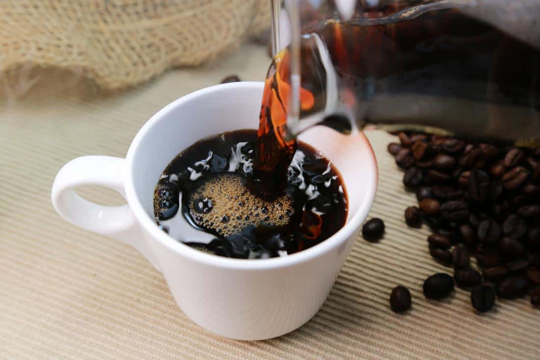 Black coffee being poured into a white mug.