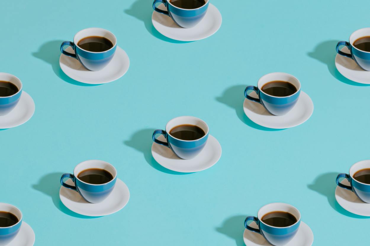 Several light blue cups of black coffee scattered on a light blue background.