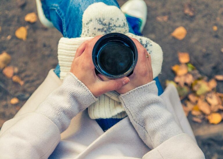 A girl in white sweater holding a cup of coffee.