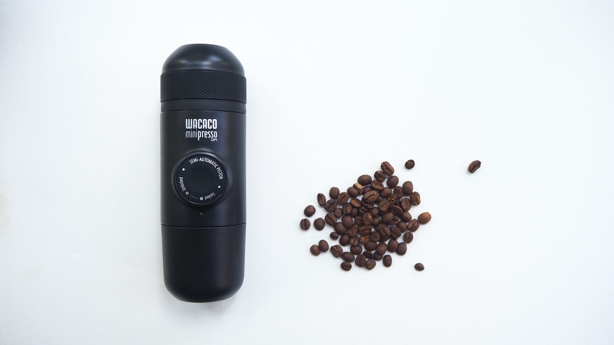 a travel coffee maker next to a pile of coffee beans