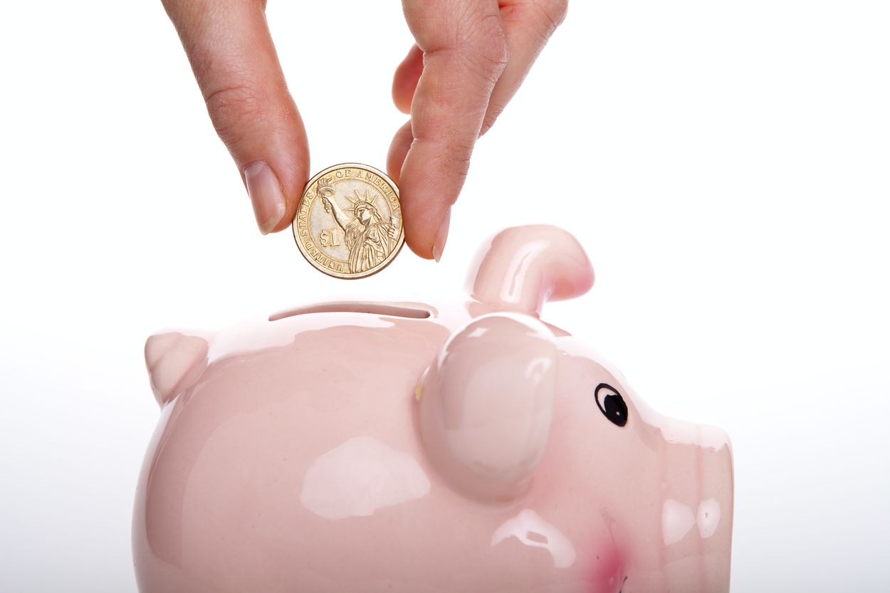 a person dropping a coin into a piggy bank