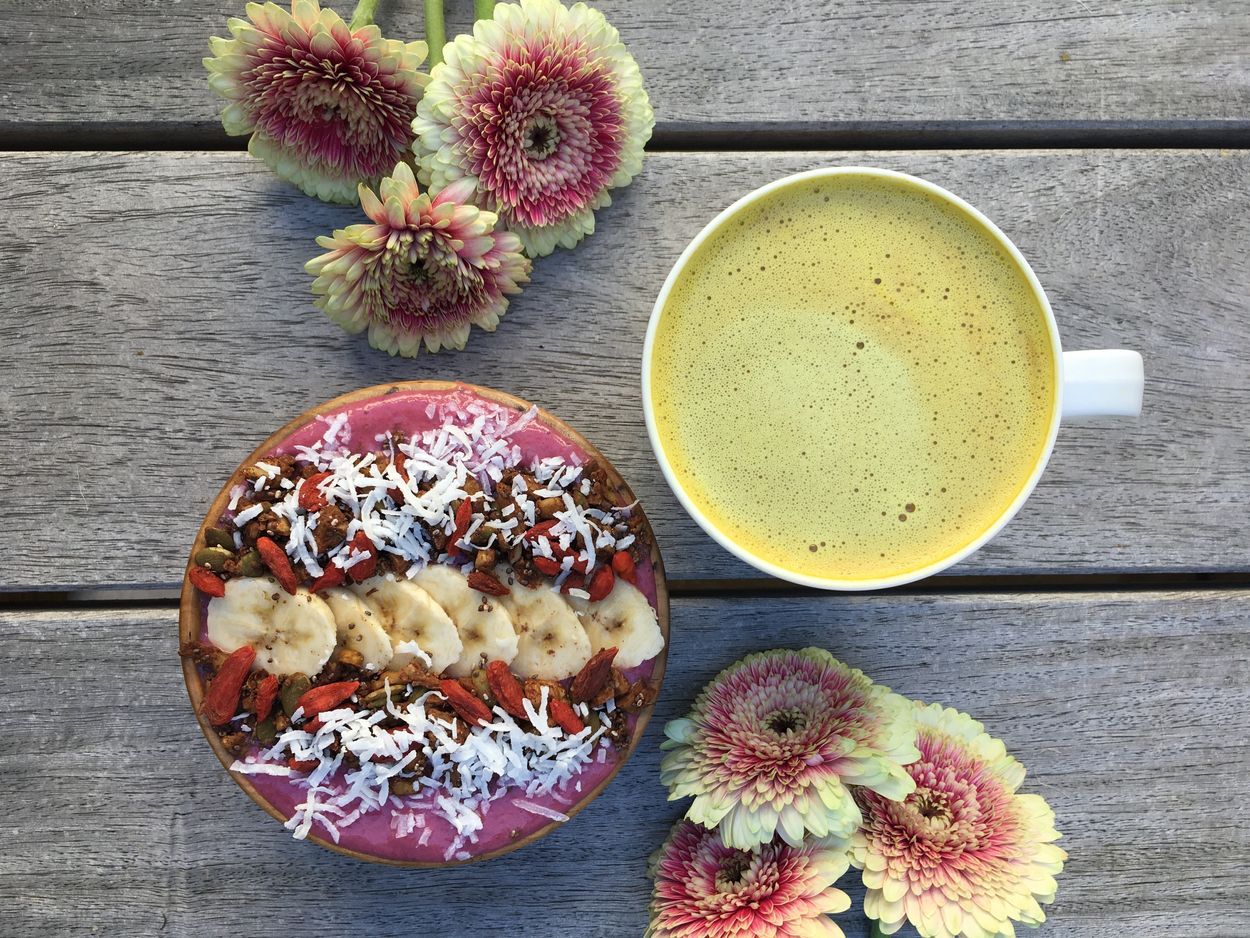 turmeric coffee next to a smoothie bowl and flowers