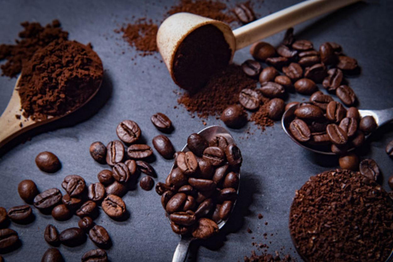 Different spoons are filled with roasted coffee beans with powder coffee on a slate stone platter background. 